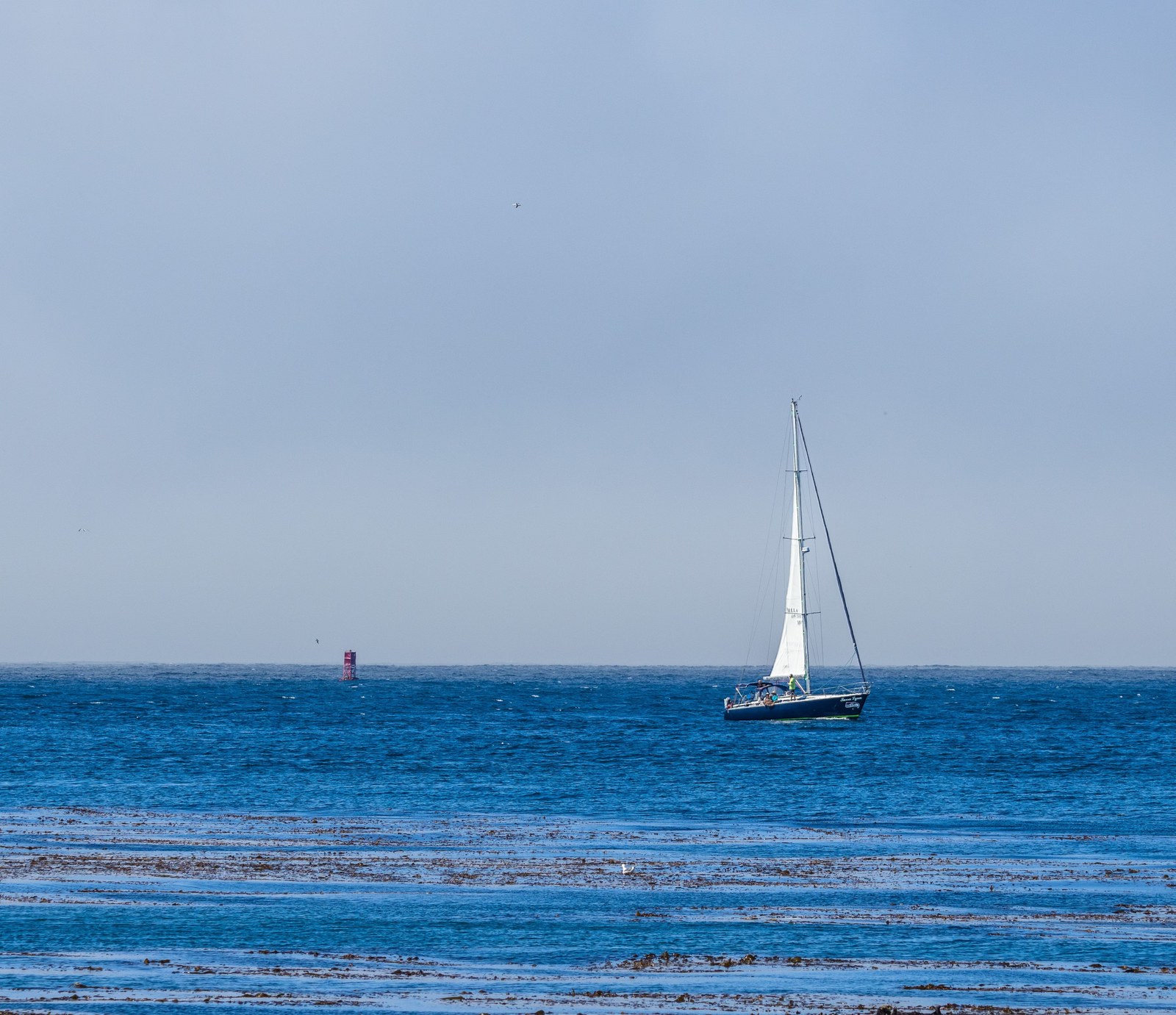 Een zeilboot vaart over een kalme blauwe zee onder een heldere lucht.